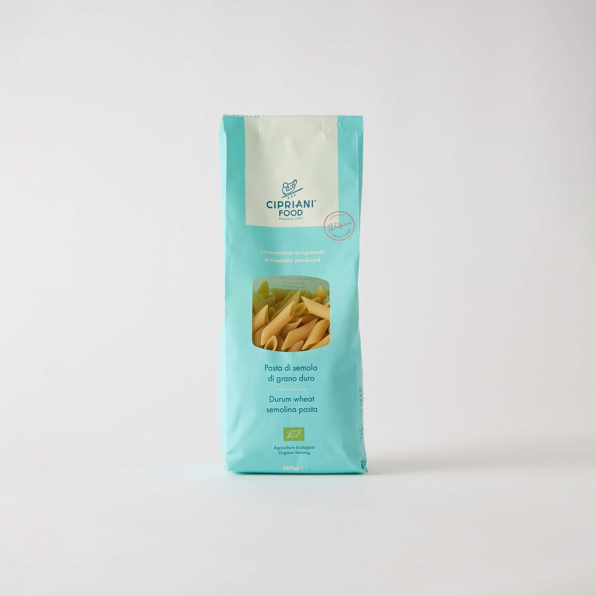 A light blue package of ATALANTA CORPORATION's CIPRIANI - ORGANIC DURUM WHEAT PENNE PASTA stands against a plain white background. The bag features a transparent window displaying the high protein index pasta inside and text detailing its Italian organic semolina content.