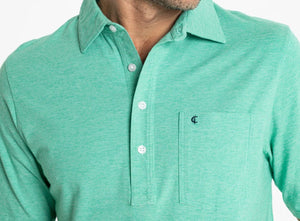 A person wears the CRIQUET Top-Shelf Players Shirt in Golf Green Microstripe with white buttons and a front pocket displaying a small embroidered logo; their face is partially out of frame.