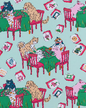 Dressed in PRINTFRESH’s Mahjong Menagerie Pajama Short Set, this person sports matching pastel organic cotton sleepwear featuring a playful cat print with tables, books, and chairs. The set includes a short-sleeve button-up shirt and shorts, both finished with light pink trim.