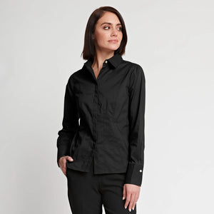 A woman with straight brown hair, wearing the HINSON WU - FRANCIS FITTED SHIRT—a tailored black button-up crafted from stretch polished cotton by HINSON WU—and black pants, stands with one hand in her pocket, gazing off to the side against a plain white background.