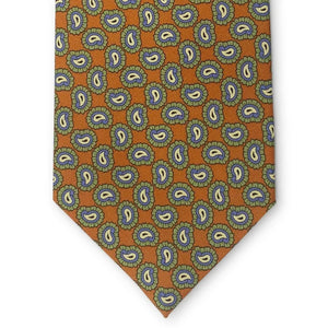 Introducing the PAGE SILK TIE IN ORANGE by BIRD DOG BAY. This expertly handmade New York tie features a vibrant orange base adorned with a repeating blue and yellow paisley pattern edged in green. With its pointed tip and solid white background, the PETER-BLAIR tie elevates classic design for a modern, sophisticated look.