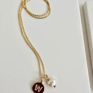 The SANDRINE FRANCE STUDIO Typewriter Initial Necklace "C" is gold-plated with a round "C" pendant and a freshwater pearl charm, handmade in NYC by SANDRINE FRANCE STUDIO and displayed on a white surface.