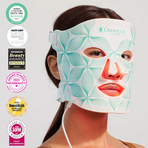 The OMNILUX - CONTOUR FACE MASK by OMNILUX, designed for skin rejuvenation and anti-aging, features red light therapy technology. It has adjustable straps, cutouts for eyes, nose, mouth, and a geometric green-white pattern on a plain white background.