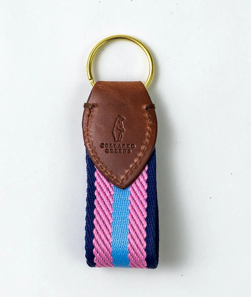 The BIRD DOG BAY COLLARED GREENS Dockside Key Chain features a sturdy cotton strap in light blue, pink, and navy stripes with a gold ring and brown leather patch—an American-made accessory for everyday style.