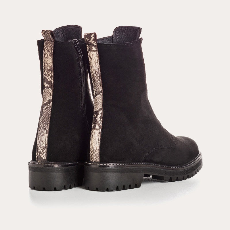 The REQINS - DUSKY SUEDE ANKLE BOOT IN NOIR features black suede leather, chunky cleated rubber soles, elastic panels on the front, and side zippers, and is displayed on a light background.