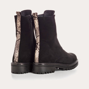 The REQINS - DUSKY SUEDE ANKLE BOOT IN NOIR features black suede leather, chunky cleated rubber soles, elastic panels on the front, and side zippers, and is displayed on a light background.