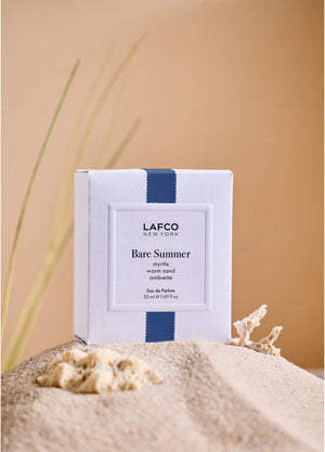 The LAFCO - FINE FRAGRANCE, BARE SUMMER 50ML perfume bottle, featuring a blue cap and displayed alongside delicate grasses, showcases its fresh and uplifting scent inspired by the sea and sand dunes. The text highlights opening, heart, and base fragrance notes that evoke the essence of summer. This vegan scent from LAFCO offers a clean, natural allure perfect for warm days.