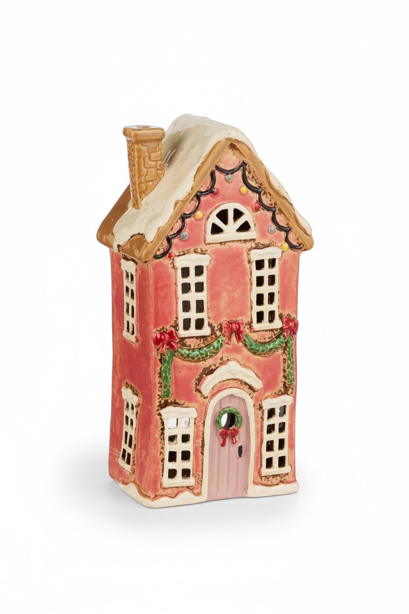 A PINK CERAMIC HOUSE tealight candle holder featuring a snow-dusted roof and festive garlands and wreaths.