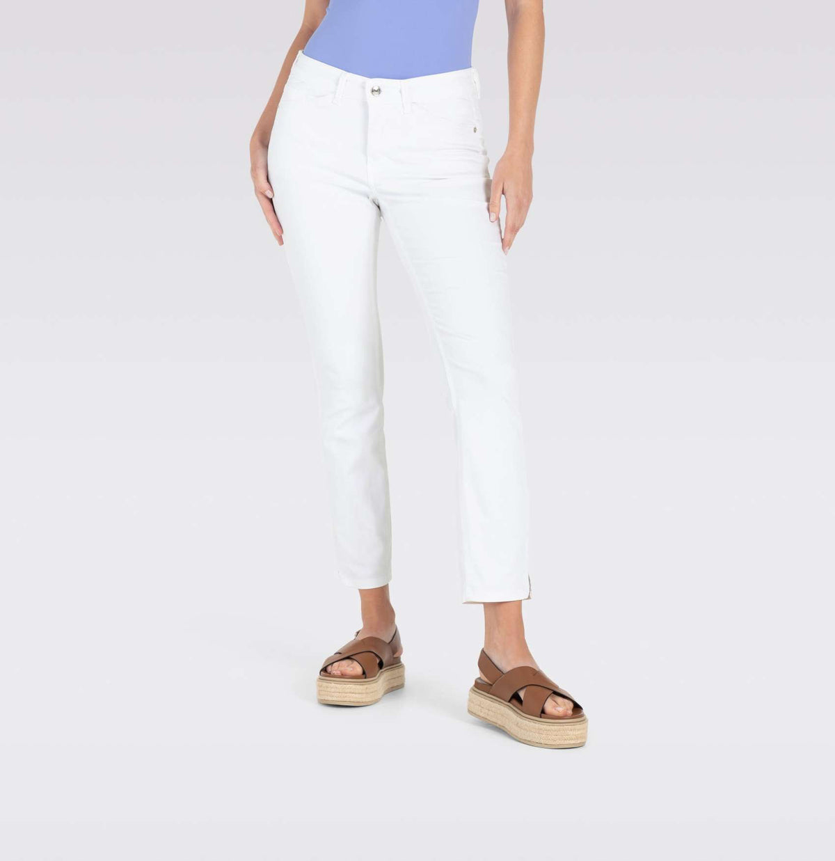 With long brown hair, a person stands against a plain backdrop wearing MAC&#39;s tan cropped jacket and MAC JEANS - DREAM SUMMER light blue slim jeans made from a comfortable modal blend. White heels complete the look as they gaze ahead with relaxed arms by their sides.