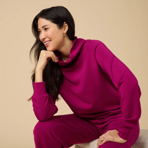A woman seen from behind wearing the fuchsia SOFTIES - DREAMTECH COWL NECK WITH PLEATED PANT set featuring a long-sleeved cowl neck top and matching pleated pants.
