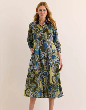 A woman stands smiling against a plain beige background, wearing the HINSON WU Martina 3/4 Sleeve Opulent Paisley Print Dress—a long-sleeve, collared, button-down dress featuring a green, blue, and brown paisley pattern and crafted from luxurious Italian polyester fabric for a fluid drape and silky hand feel.