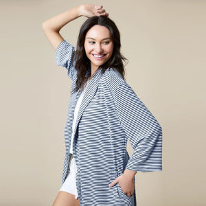 A woman wears a SOFTIES - DREAM SHAWL COLLAR ROBE in pink and white stripes, featuring a shawl collar, a tie waist, and three-quarter length sleeves.