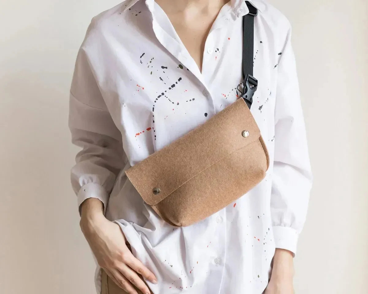 A person wearing a tan felt belt bag with a black strap over a white button-down shirt.
