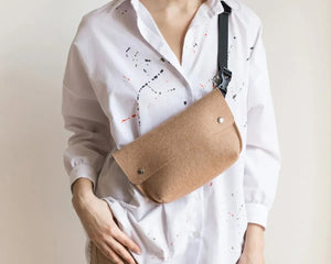 The WOOLBERRY - FELTED WOOL BELT BAG by WOOLBERRY is a small green belt bag crafted from felted wool, featuring a flap secured by two silver snap buttons, and is displayed against a white background.