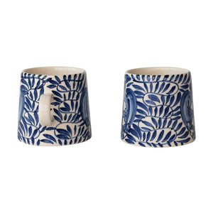 The CREATIVE COOP CREAM AND BLUE HAND-PAINTED STONEWARE MUG features a blue floral and leaf design on white, a handle, tapered shape, and glossy finish—bringing artisanal charm to your daily coffee.