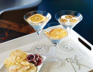 A transparent, tall bag containing neatly stacked dried orange slices. The bag is tied at the top with a clear ribbon. The product label reads "DARDIMANS - CRISPY ORANGE SLICES," hinting at the fresh orange flavor packed with vitamin C. The background is a light textured surface, giving a rustic appearance.