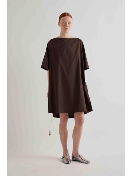 A person with straight red hair stands against a plain light background, wearing the MEIMEIJ oversized cotton shift dress in black by MEIMEIJ and silver flat shoes.