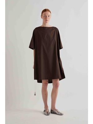 A person with straight red hair stands against a plain light background, wearing the MEIMEIJ oversized cotton shift dress in black by MEIMEIJ and silver flat shoes.