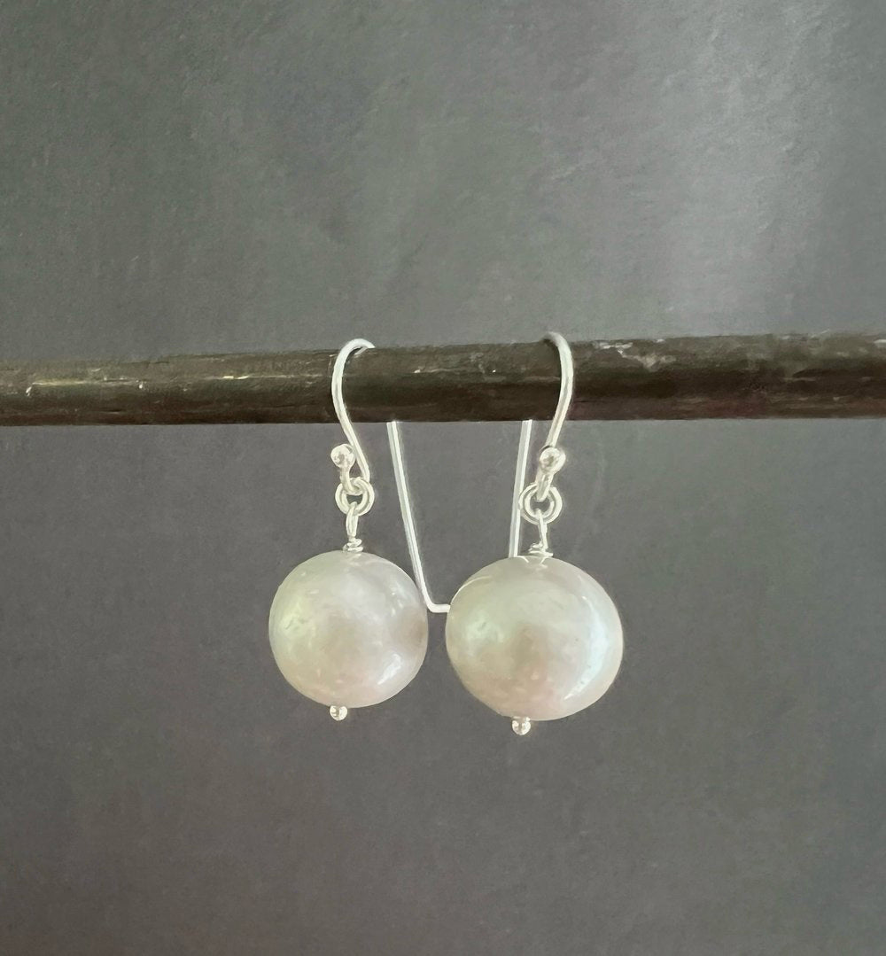 ANN LIGHTFOOT FRESHWATER PEARL DROP EARRINGS feature a single round white freshwater pearl on sterling silver earwires, shown hanging from a dark rod against a white background.