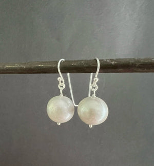 ANN LIGHTFOOT FRESHWATER PEARL DROP EARRINGS feature a single round white freshwater pearl on sterling silver earwires, shown hanging from a dark rod against a white background.