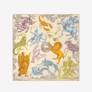 A person with long dark hair wears the INOUI EDITIONS Astrologie Scarf—a silk modal blend adorned with intricate zodiac signs—over a white strapless top, set against a plain white background.