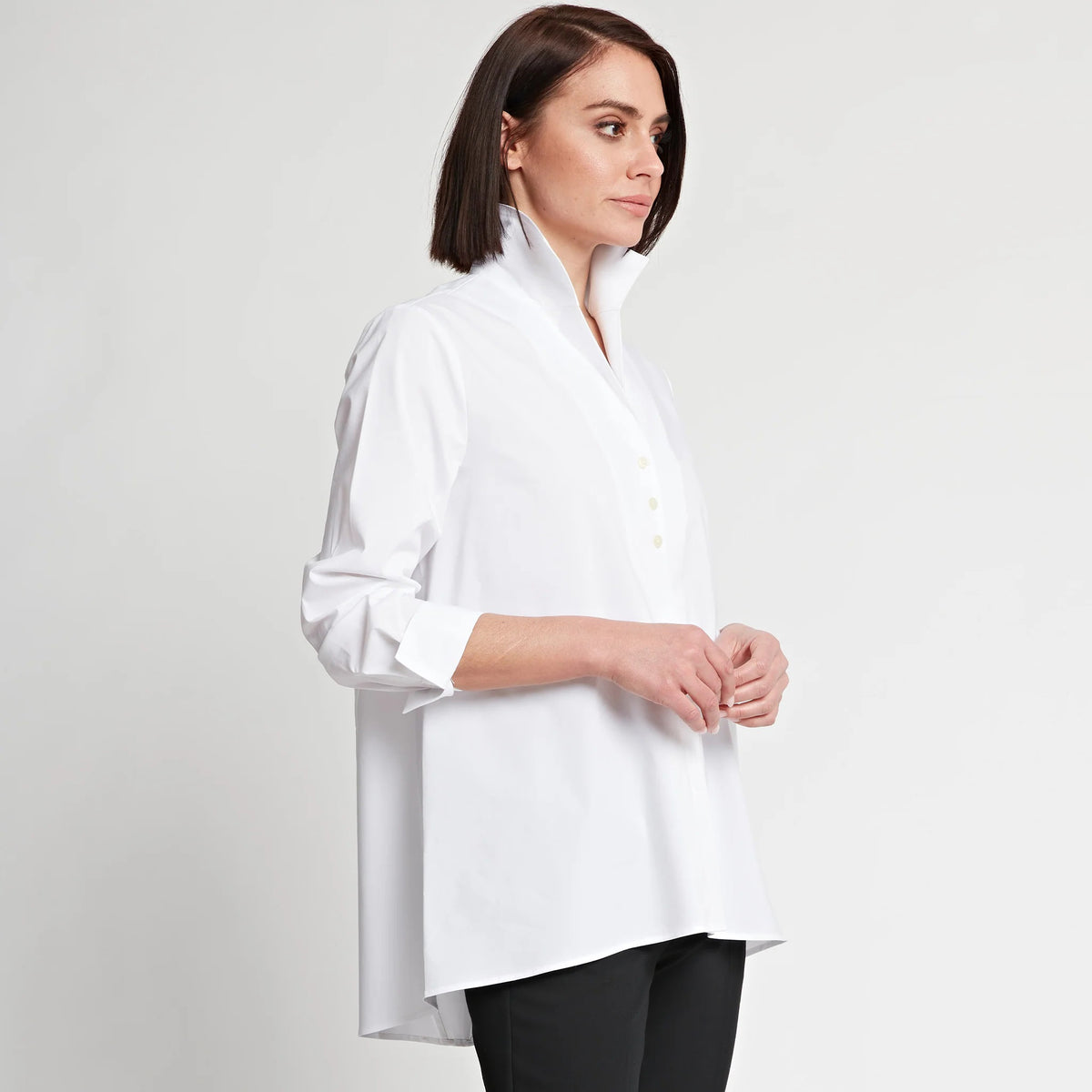 A person with short brown hair stands against a plain white background, wearing the HINSON WU - BETTY LONG SLEEVE TUNIC with the sleeves rolled up to the elbows and black pants. One hand is tucked into their pocket, and they look confidently at the camera.