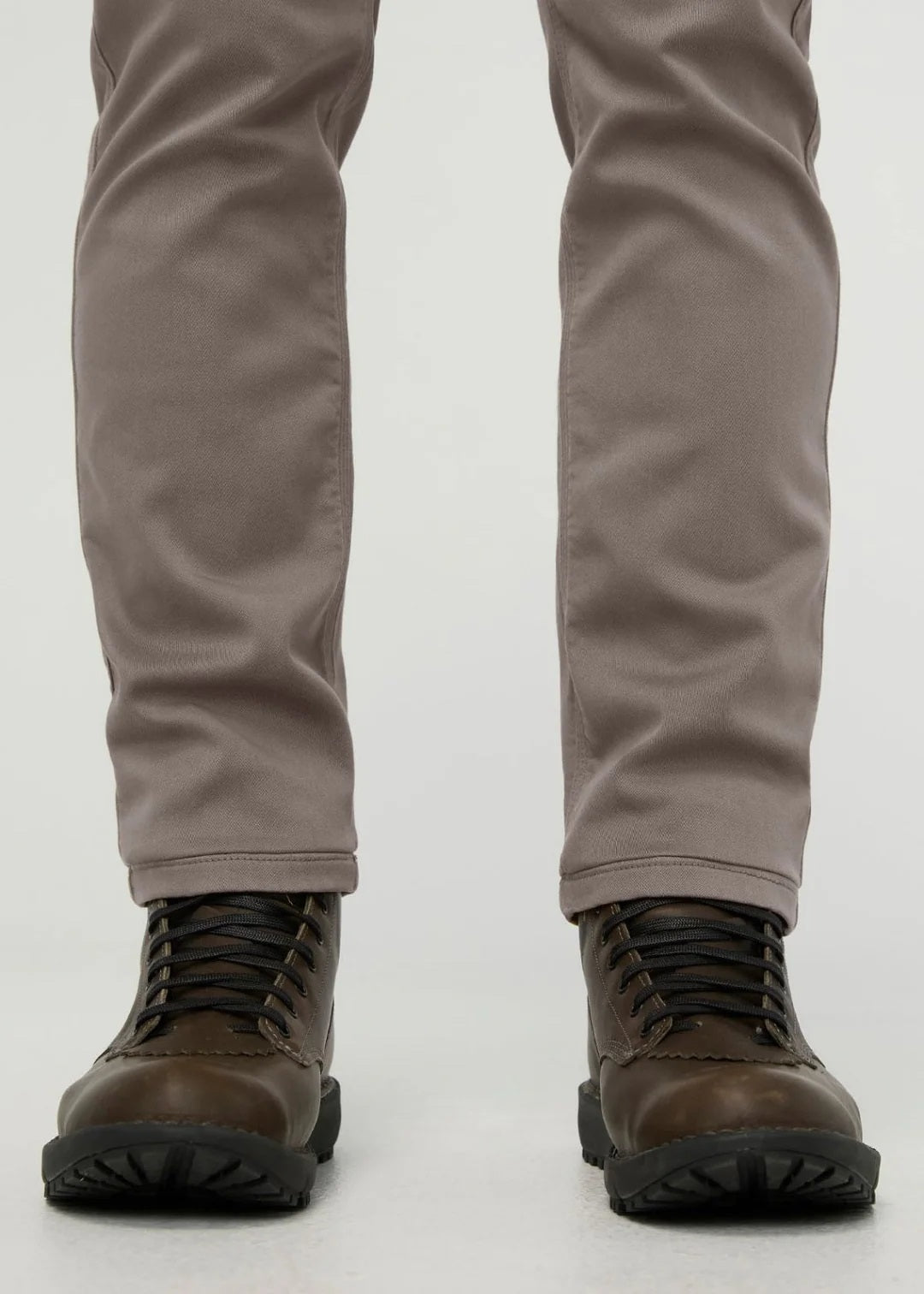 Close-up of the back of a person wearing DUER No Sweat Athletic Taper Pants in Stone, featuring two back pockets and a tan leather DUER patch on the waistband. They're also wearing a black shirt.