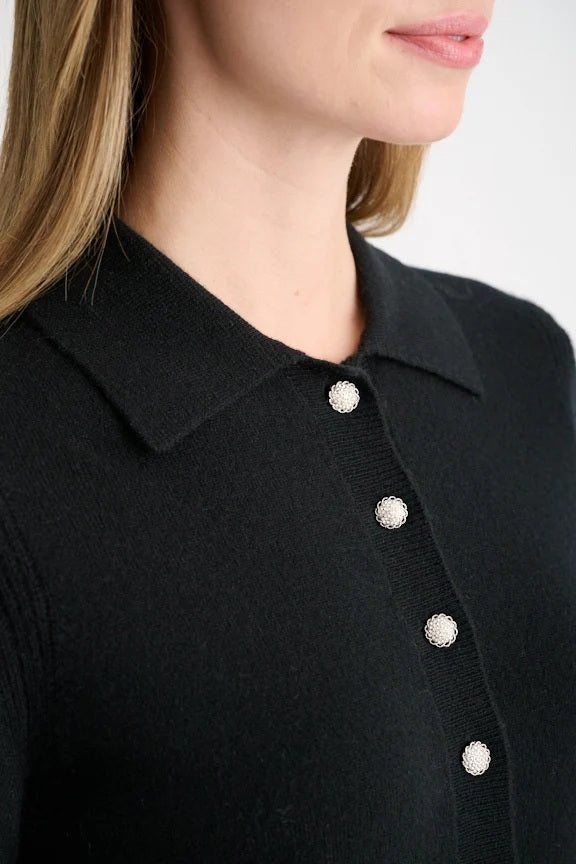 A person wearing the KINROSS CASHMERE Crystal Button Cashmere Polo in black by KINROSS, paired with blue jeans, stands facing forward against a plain white background.