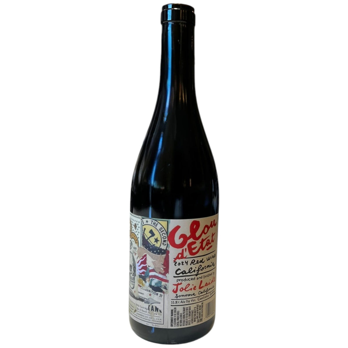 A bottle of JOLIE-LAIDE ’GLOU D’ETAT’ 2024 from WINE: KELLOGG SELECTIONS, featuring a colorful label, sits on a white table in front of shelves stocked with assorted wine bottles in a store.