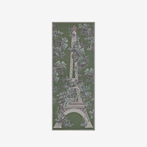 A person with short hair wears a long black dress and the INOUI EDITIONS 1889 WOOL SCAR FIN KHAKI scarf by INOUI—a green patterned accessory featuring intricate floral and geometric designs, crafted from 100% wool in India—while standing against a plain white background.