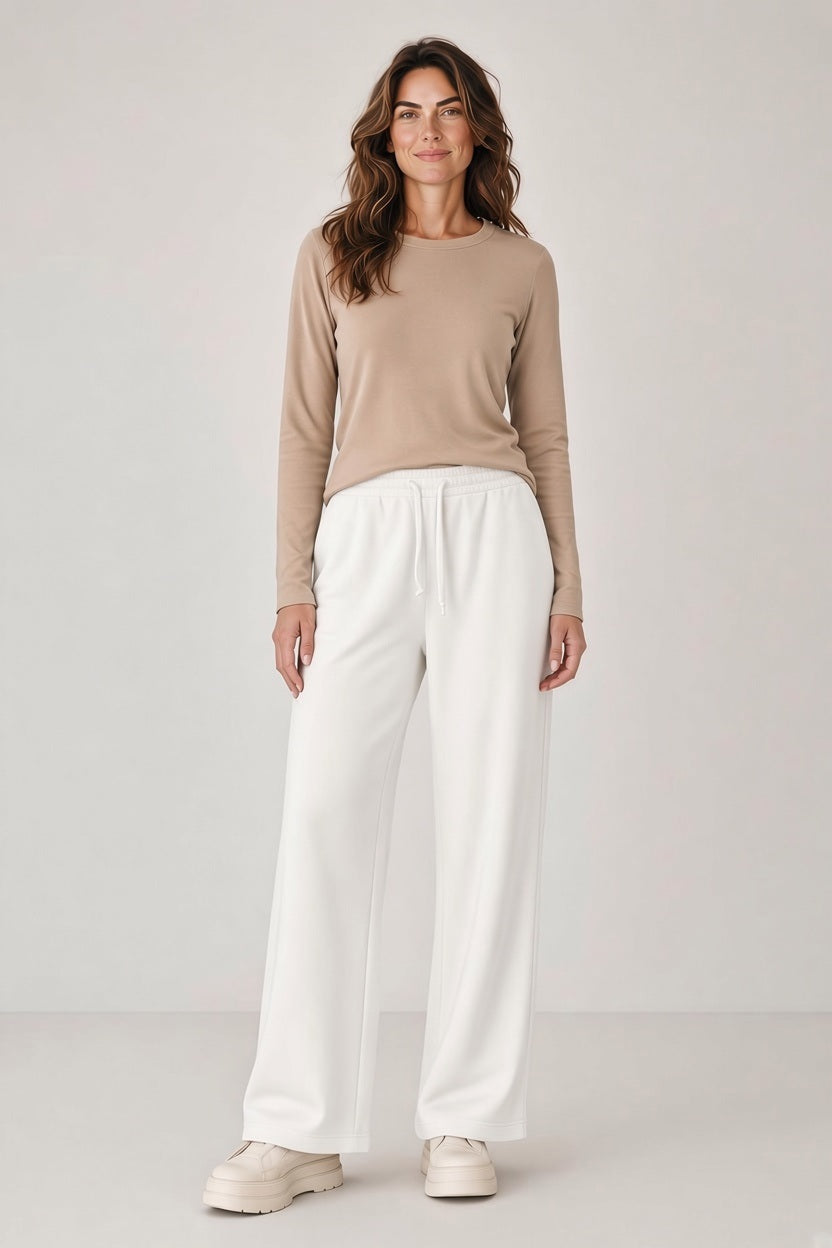 A woman wearing a long-sleeved tan shirt and SAVE THE DUCK - IZUMI PULL ON DRAWSTRING WIDE LEG PANT IN CLOUD WHITE with chunky white platform sneakers.