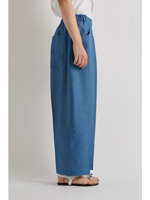 A person stands against a plain light background, cropped at the shoulders, wearing MEIMEIJ Pull On Barrel Pant in Cerulean with an elastic waistband, paired with a white shirt and sandals.