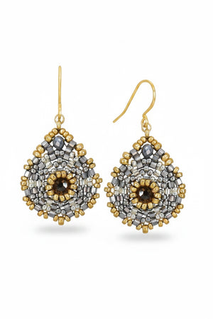 Introducing the MIGUEL ASES Miyuke Crystal Pyrite Earrings: elegant, teardrop-shaped earrings featuring a central dark stone surrounded by silver and gold beads in a symmetrical design, complete with hook attachments. Crafted by MIGUEL ASES, INC., they exude handcrafted sophistication.