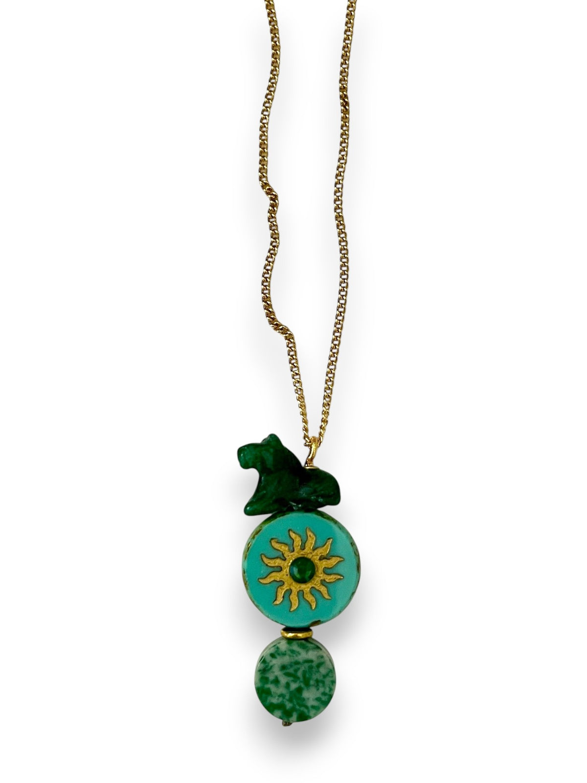 The SANDRINE FRANCE STUDIO - COMPANION AUSTIN NECKLACE by SANDRINE FRANCE STUDIO features a gold chain adorned with three green pendants: a small abstract shape, a jade round disk accented with a gold sun motif, and an oval bead with a marbled pattern—each detail showcasing the artistry of handmade NYC craftsmanship.