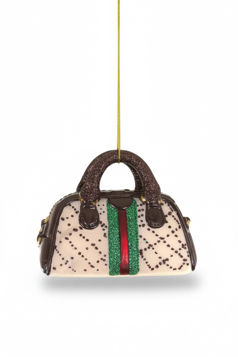 SMALL LUXURY HANDBAG ORNAMENT by Cody Foster, a 2.5-inch tall miniature handbag with a cream-colored body, brown handles, and a decorative green and red stripe down the center.