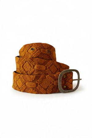The JENNY KRAUSS - TERRACOTTA EMBROIDERED WOOL BELT, handcrafted in Peru, features a diamond embroidery pattern, metal buckle, and textured brown wool fabric, neatly coiled on a white surface.