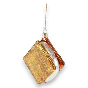 The CODY FOSTER S'MORE ORNAMENT features glittery gold graham crackers, a white marshmallow, and brown chocolate—hanging by a string, it's a perfect collectible or a thoughtful gift for design lovers.
