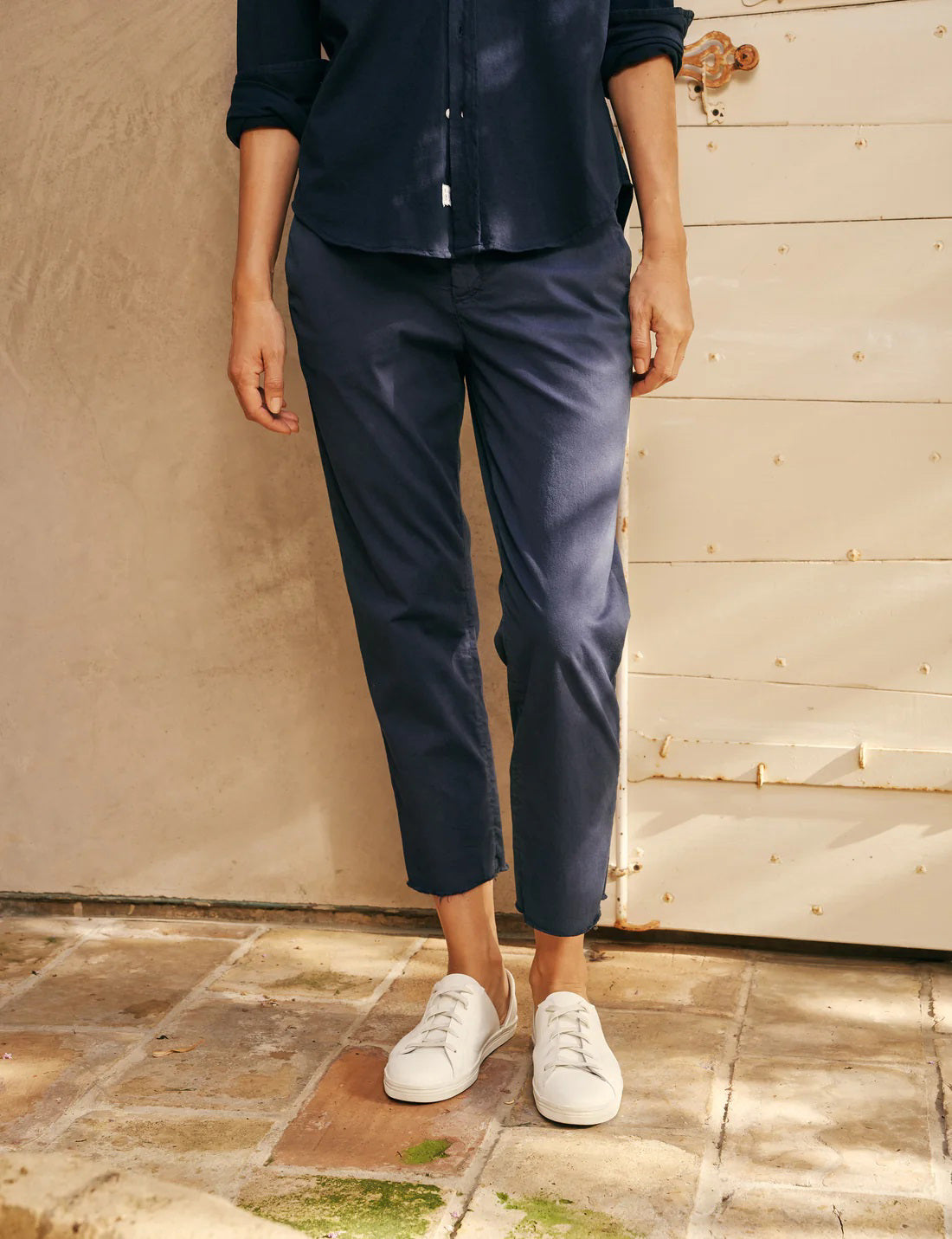 A pair of FRANK &amp; EILEEN’s THE WICKLOW Italian Chinos in Performance Twill, featuring a navy blue color, straight legs, and raw unfinished hems, is laid flat on a light textured background for an Italy-meets-California vibe.