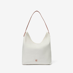 The INOUI EDITIONS - HAWAII CAMPUS CANVAS BAG highlights a tropical landscape in earthy tones with palm trees and foliage, offering a painterly vintage charm. Its slouchy design and single leather strap elegantly combine style and function against a plain white background.