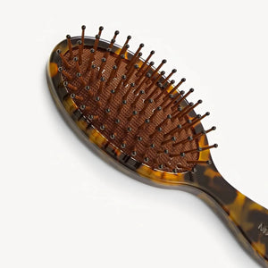 A close-up of the MACHETE Petite Travel Detangling Hair Brush in Tortoise, crafted from Italian acetate with a cushioned base and rounded bristle tips, set against a plain white background.