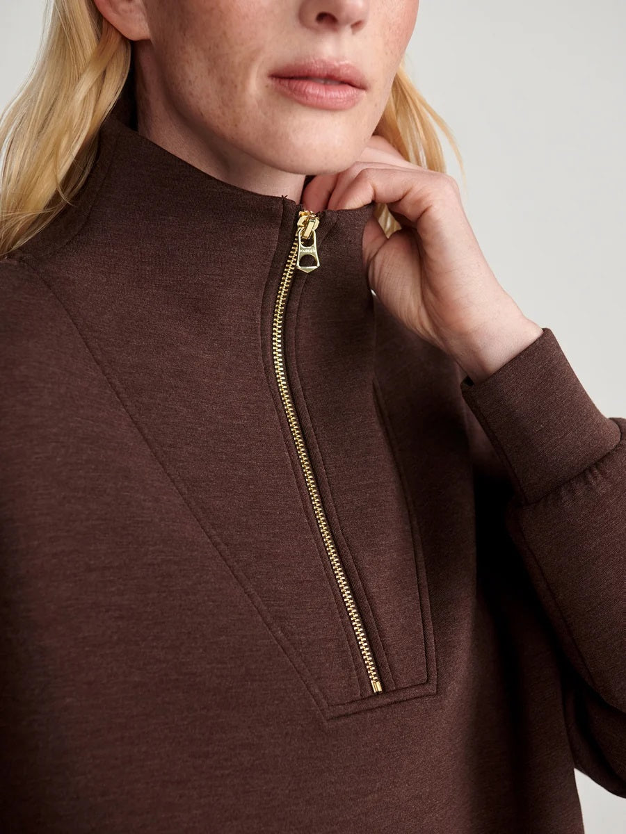 A person wears an oversized, dark brown VARLEY - HAWLEY HALF-ZIP SWEATSHIRT IN COFFEE BEAN MARL with a gold zipper.