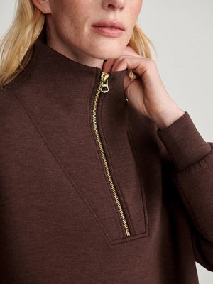 A person wears an oversized, dark brown VARLEY - HAWLEY HALF-ZIP SWEATSHIRT IN COFFEE BEAN MARL with a gold zipper.