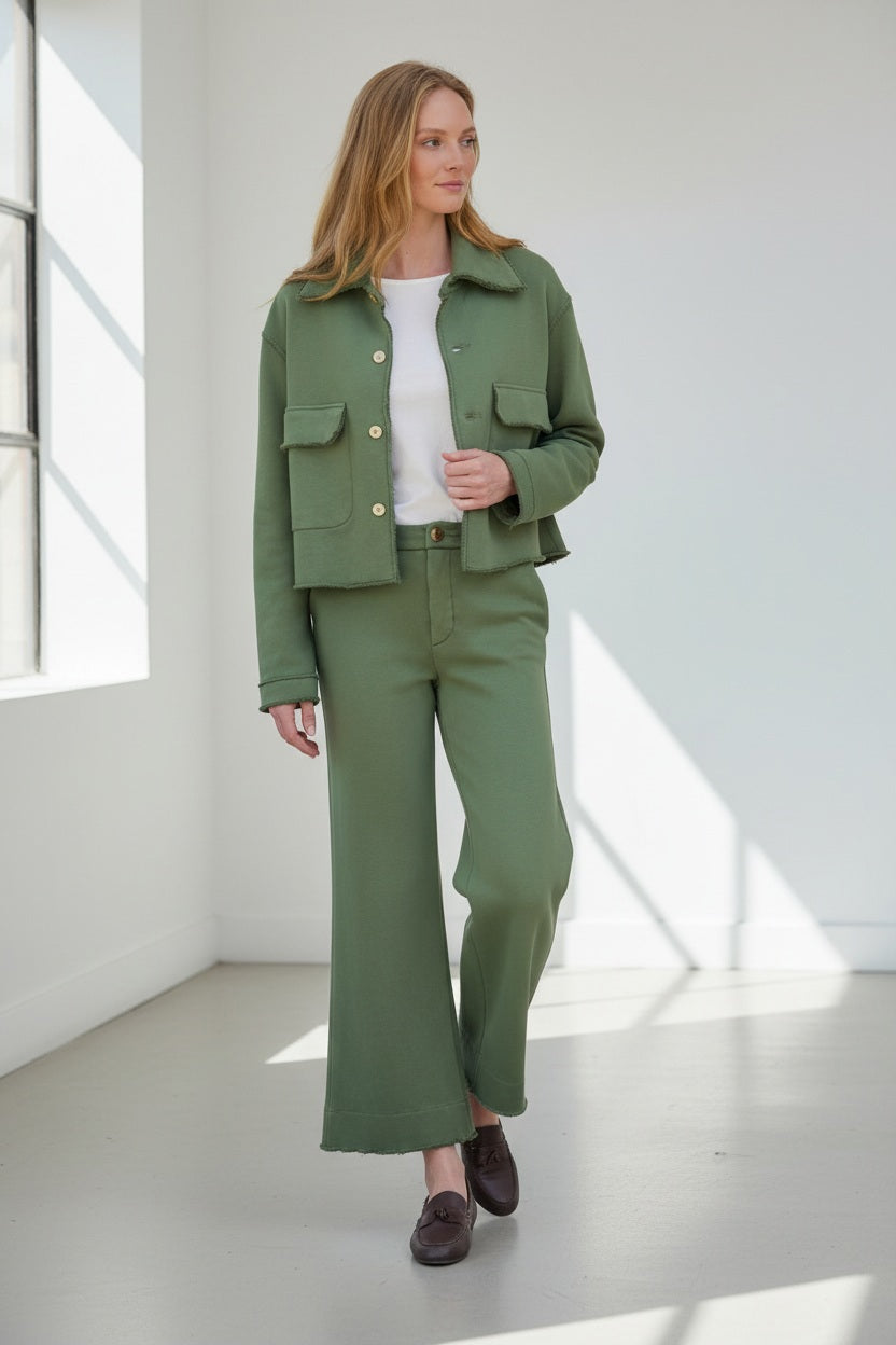 Fearrington Village model wearing green wide-leg Riley trouser sweatpants and matching jacket in a rustic setting.