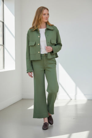 Fearrington Village model wearing green wide-leg Riley trouser sweatpants and matching jacket in a rustic setting.