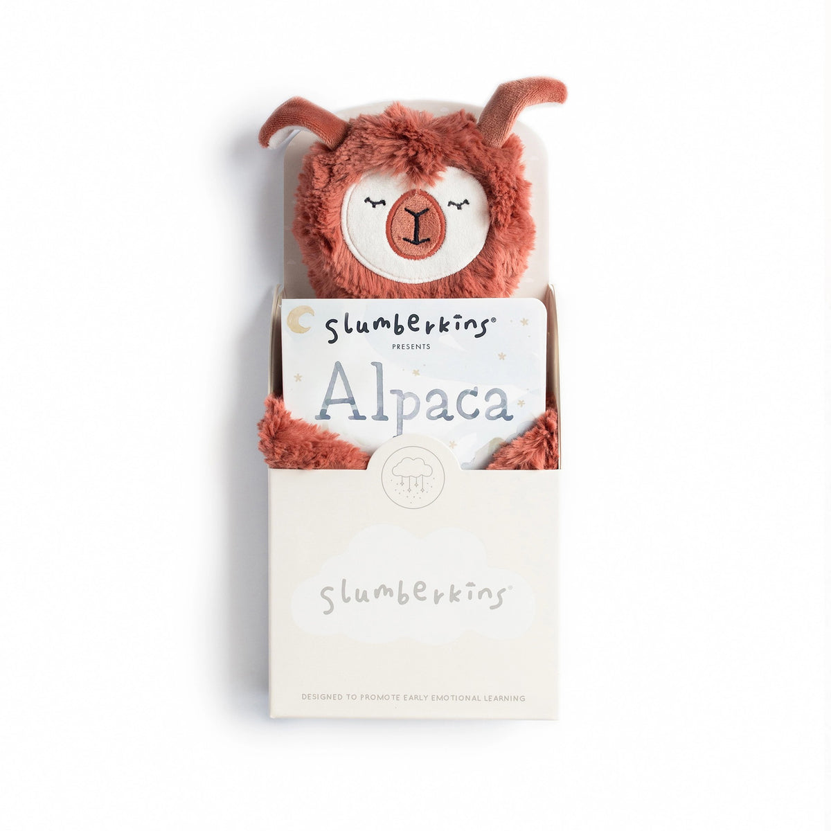 A cuddly SLUMBERKINS Alpaca Snuggler in rust is nestled in a white box adorned with the SLUMBERKINS logo. It includes a book titled "Alpaca," aimed at enhancing early emotional learning and managing anxiety.