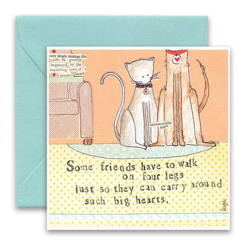 The CURLY GIRL DESIGNS - FOUR LEGS GREETING CARD from CURLY GIRL DESIGN, INC features two adorable illustrated cats, one gray and one brown, sitting beside an orange sofa. The card's text reads, "Some friends have to walk on four legs just so they can carry around such big hearts." This charming collage art card comes with a blue envelope.