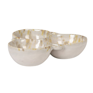 A rustic flat lay features the CREATIVE COOP 3-SECTION STONEWARE BOWL IN CREAM AND GREEN filled with spices, dried artichoke, garlic bulbs, vintage metal spoons, and assorted nuts on a textured beige surface.