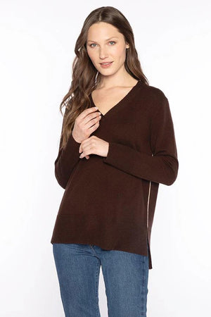 A woman with long brown hair models the KINROSS CASHMERE Hi Low Side Piped Easy Vee Neck Sweater by KINROSS, paired with blue jeans, standing against a plain white background and smiling slightly at the camera.