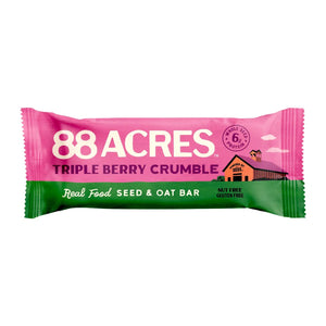 An 88 ACRES - TRIPPLE BERRY CRUMBLE Seed + Oat Bar rests on a light wooden surface, with its package partially open to show a portion of the nut-free and vegan granola bar inside. The packaging is white, featuring a vibrant purple section that displays the product name and various icons.