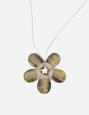 A mannequin showcases the ANN LIGHTFOOT - FLOURITE FLOWER NECKLACE, featuring a large gold and brown flower-shaped pendant, elegantly paired with a braided light grey shawl. The neutral brown fabric background highlights the refined beauty of this adjustable necklace by ANN LIGHTFOOT.